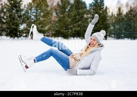 ragazza divertente che cade mentre pattina sul ghiaccio alla pista invernale Foto Stock
