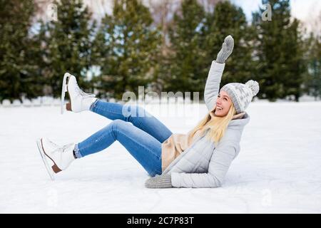 giovane donna che cade mentre pattina sul ghiaccio alla pista invernale Foto Stock