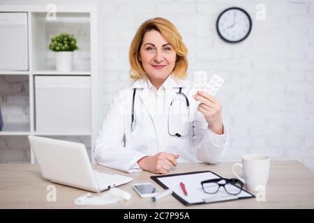 medico femminile maturo che mostra pillole in ufficio moderno o farmacia negozio Foto Stock