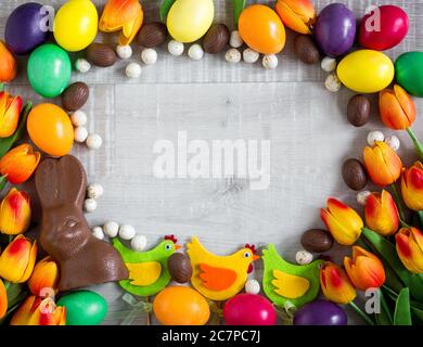 Sfondo cornice di Pasqua - primo piano di uova colorate, pulcini decorativi, tulipani, coniglietto di cioccolato e dolci Foto Stock