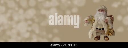 Babbo Natale giocattolo in abiti d'oro con una borsa piena di regali. Banner con Babbo Natale isolato su sfondo sfocato, copia spazio per il tuo testo. Natale Foto Stock