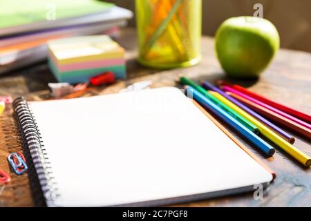 Torna a scuola: Nota libro, matite, loupa, mela verde su tavolo di legno Foto Stock
