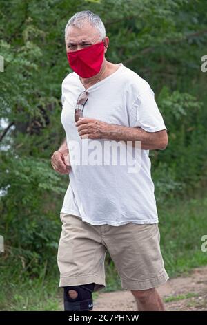 Un uomo anziano di mezza età che indossa una maschera rossa brillante corre lungo un sentiero vicino alla Marina di Bayside a Queens, New York City. Foto Stock
