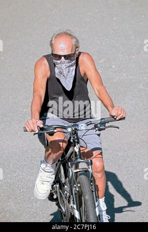 Un uomo di mezza età che indossa una bandana corre in bicicletta su un sentiero in un parco a Flushing, Queens, New York City. Foto Stock