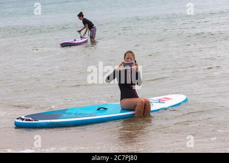 Poole, Dorset UK. 19 luglio 2020. Tempo in Gran Bretagna: Un inizio grigio e frizzante della giornata alle spiagge di Poole. Donna seduta sul paddle board in mare scattando una foto. Credit: Carolyn Jenkins/Alamy Live News Foto Stock