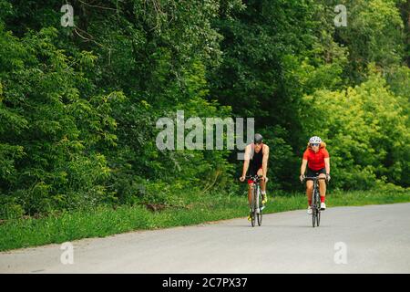 Coppia di ciclisti professionisti in bicicletta su strada attraverso una foresta in una giornata estiva Foto Stock
