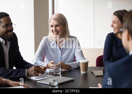 I compagni di lavoro allegri e multietnici ridono durante le riunioni di gruppo nella sala riunioni dell'ufficio Foto Stock