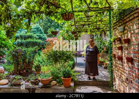 Tbilisi , Georgia - 25 agosto 2019 : una donna anziana che si posa nel giardino di casa sua nella città vecchia Foto Stock