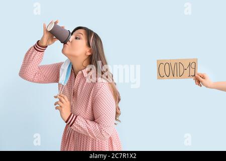 Giovane donna con maschera protettiva e tazza di caffè su sfondo colorato. Concetto di epidemia di coronavirus Foto Stock