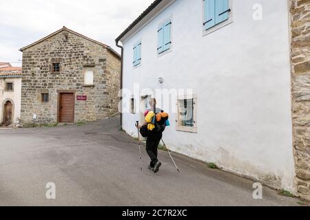 Donna escursionista con bastoni e uno zaino trekking ld casa tradizionale con porta blu chiaro e persiane nel villaggio di Hrastovlje, slovenia Foto Stock