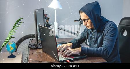 Man hacker in una cappa sono la programmazione del codice virus su un computer portatile. Il concetto di frode su Internet e di hacking dei dati personali Foto Stock