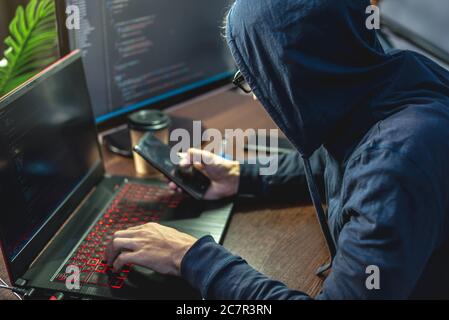 Man hacker nel cappuccio sta programmando il codice del virus alla tastiera per il portatile. Il concetto di frode su Internet e di hacking dei dati personali Foto Stock