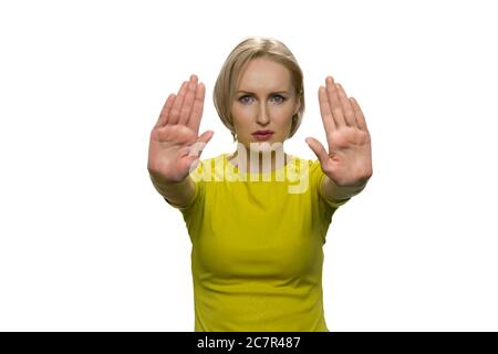 Giovane donna in tleneck giallo che fa il gesto di arresto con entrambe le mani su sfondo bianco. Foto Stock