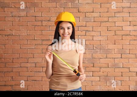 Giovane donna con metro a nastro vicino muro di mattoni Foto Stock