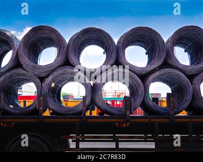 Bobine di filo metallico in acciaio sul rimorchio di autocarro nella zona industriale. Il carrello riceve l'asta metallica in acciaio dall'area di disriempimento del contenitore di magazzino. Foto Stock