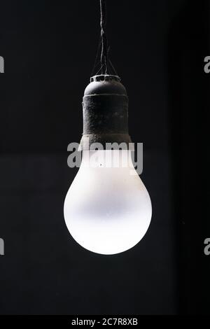 Immagine isolata verticale di una lampadina bianca appesa su un sfondo nero Foto Stock