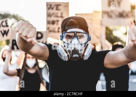 Il giovane uomo che fa il simbolo del pugno per la protesta generale sulla strada - i dimostranti che indossano le maschere del viso e del gas durante la campagna di lotta - fuoco sulle res indossabili Foto Stock