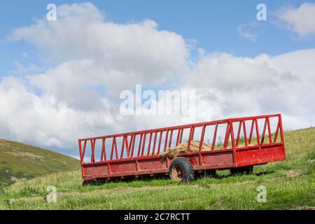 Un carro da fieno di fattoria dipinto di rosso su una collina nel periodo estivo Foto Stock