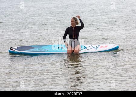 Poole, Dorset UK. 19 luglio 2020. Tempo in Gran Bretagna: Un inizio grigio e frizzante della giornata alle spiagge di Poole. Donna seduta sul paddle board in mare scattando una foto. Credit: Carolyn Jenkins/Alamy Live News Foto Stock