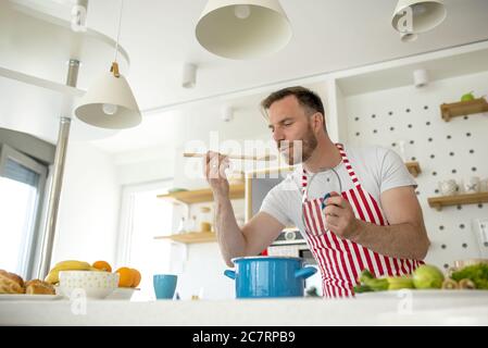 Uomo che indossa un grembiule bianco con linee rosse e cucina qualcosa in  cucina Foto stock - Alamy