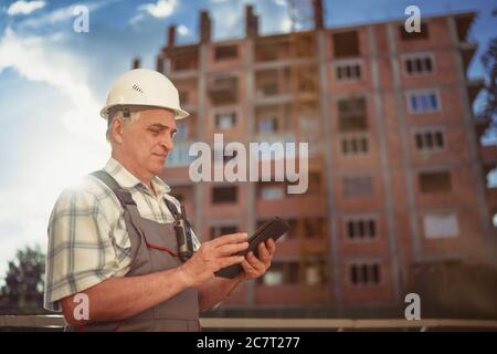 Responsabile della costruzione che controlla il sito dell'edificio con un tablet pc al tramonto Foto Stock