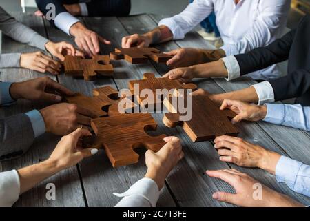 Il team di persone di affari seduti intorno al tavolo di riunione e l'assemblaggio di pezzi di puzzle di legno di cooperazione unità idee concetto Foto Stock