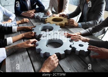 Gruppo di uomini d'affari che si uniscono a ingranaggi color argento e oro sul tavolo sul luogo di lavoro Foto Stock