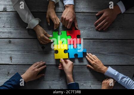 Il team di persone di affari seduti intorno al tavolo di riunione e l'assemblaggio di pezzi di puzzle a colori unità idee di cooperazione concetto Foto Stock