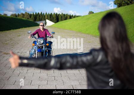 hitchhiking concetto - donna che si accocciano uomo in moto sulla strada Foto Stock