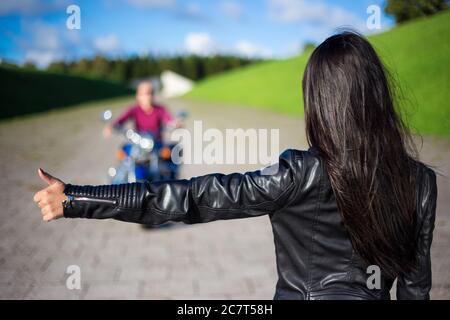 hitchhiking concetto - vista posteriore di giovane donna che si accocciano uomo sulla moto sulla strada Foto Stock