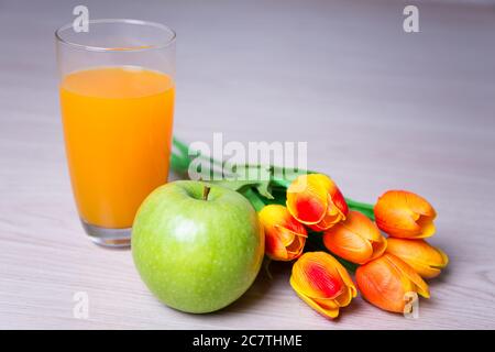 bicchiere di succo, mela e tulipani su tavola di legno Foto Stock