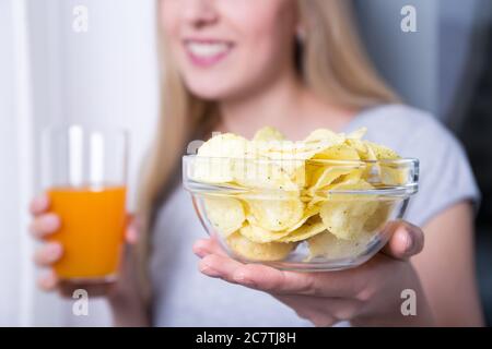 ciotola con patatine e bicchiere di succo in mani femminili Foto Stock