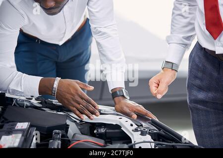 cliente africano e venditore caucasico hanno aperto il cofano dell'auto e discusso tutte le sfumature riguardanti l'auto. in concessionaria Foto Stock