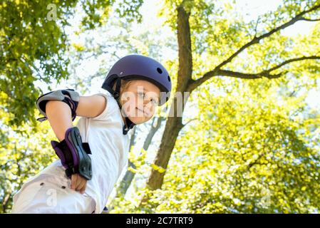 Scatto ad angolo basso di una bambina che indossa un casco e gli attrezzi di protezione sorridono in un parco Foto Stock