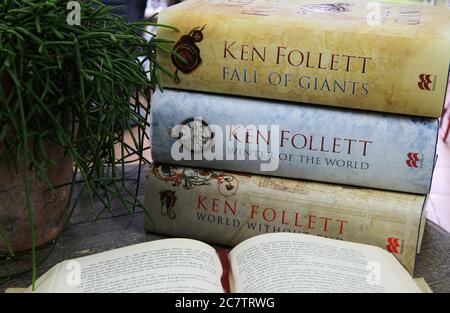 Viersen. Germania - 9 luglio. 2020: Vista su tavola di legno con libro aperto, pila di libri di romanzi Ken Follett e pianta verde Foto Stock
