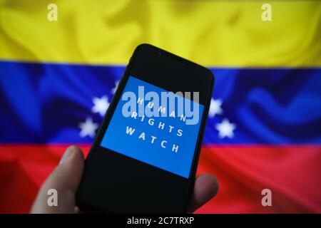 Viersen, Germania - 9 luglio. 2020: Visualizzazione sullo schermo dello smartphone con il logo dell'organizzazione di orologi per i diritti umani. Sfondo bandiera Venezuela sfocato.( Foto Stock