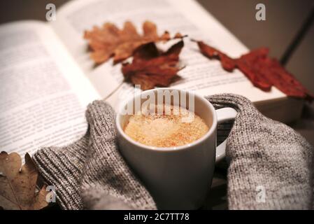Messa a fuoco selettiva di una tazza di caffè e sciarpa con un libro aperto e foglie di autunno sfondo Foto Stock