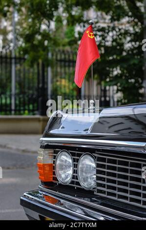 Auto nera classica con la bandiera dell'URSS sul cofano. Frammento di un'auto d'epoca sulla strada. Foto Stock