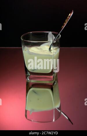 Yogurt greco in un vaso di vetro con cucchiaio su fondo rosso e nero primo piano. Foto Stock