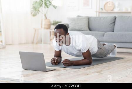 Giovane uomo nero che si esercita a casa, utilizzando il computer portatile Foto Stock