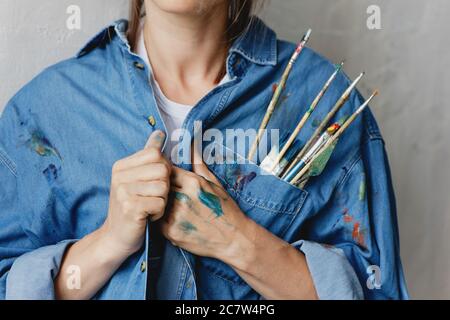 Immagine tagliata di donna con pennelli e coltello per la pittura messi nella tasca della sua camicia in denim. Foto Stock