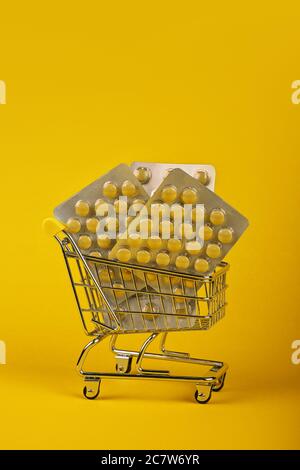 Primo piano diversi blister confezioni di pillole in piccolo carrello di shopping su sfondo giallo, concetto di online medicina ordine di consegna, angolo basso Foto Stock