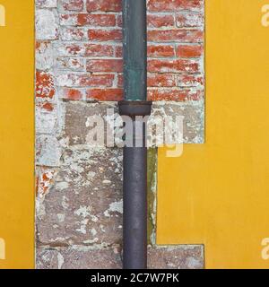 Vecchio rame arrugginito e tubo discendente in ghisa contro un muro di mattoni e intonaco. Foto Stock