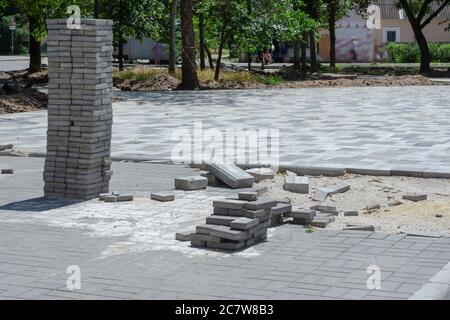 Il processo di posa di lastre di pavimentazione in un parco cittadino. Lastre di pavimentazione grigie piegate in una colonna. Ricostruzione dell'area di intrattenimento e ricreazione di Foto Stock
