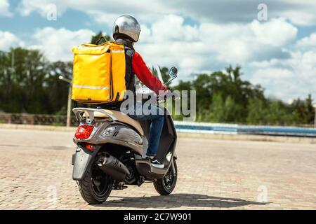 Corriere con zaino Riding Scooter consegna pasti in città, Back-View Foto Stock