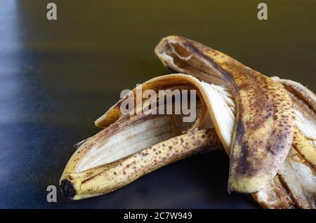 Foto dettagliata scartata buccia di banana su sfondo nero. La buccia di banane sopramature con macchie marroni. Rifiuti alimentari. Primo piano. Messa a fuoco selettiva. Foto Stock