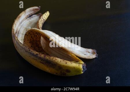 Foto dettagliata scartata buccia di banana su sfondo nero. Buccia di banana eccessivamente matura con macchie marroni. Rifiuti alimentari. Primo piano. Messa a fuoco selettiva. Foto Stock