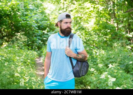 uomo bearded sguardo confidente. uomo bearded bruna indossa il cappuccio in foresta sullo sfondo degli alberi. uomo bruna bruno bearded brutale con lo zaino. ragazzo maturo con la barba in legno. bel giorno d'estate. Foto Stock