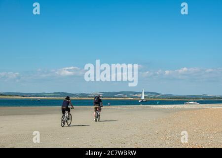 Due ciclisti su una spiaggia vuota nel Sussex occidentale Foto Stock