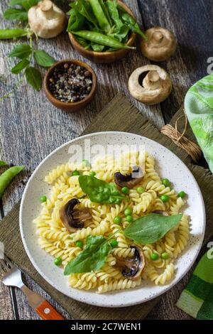 Cibo sano. Pasta fusilli fatta in casa con piselli verdi e champignons alla griglia su un tavolo di legno. Foto Stock